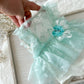 Light mint green lace newborn romper with a flower detail held by a hand on a light wooden surface.