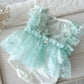 Light mint green lace baby romper with lace and ruffles on a wooden surface.