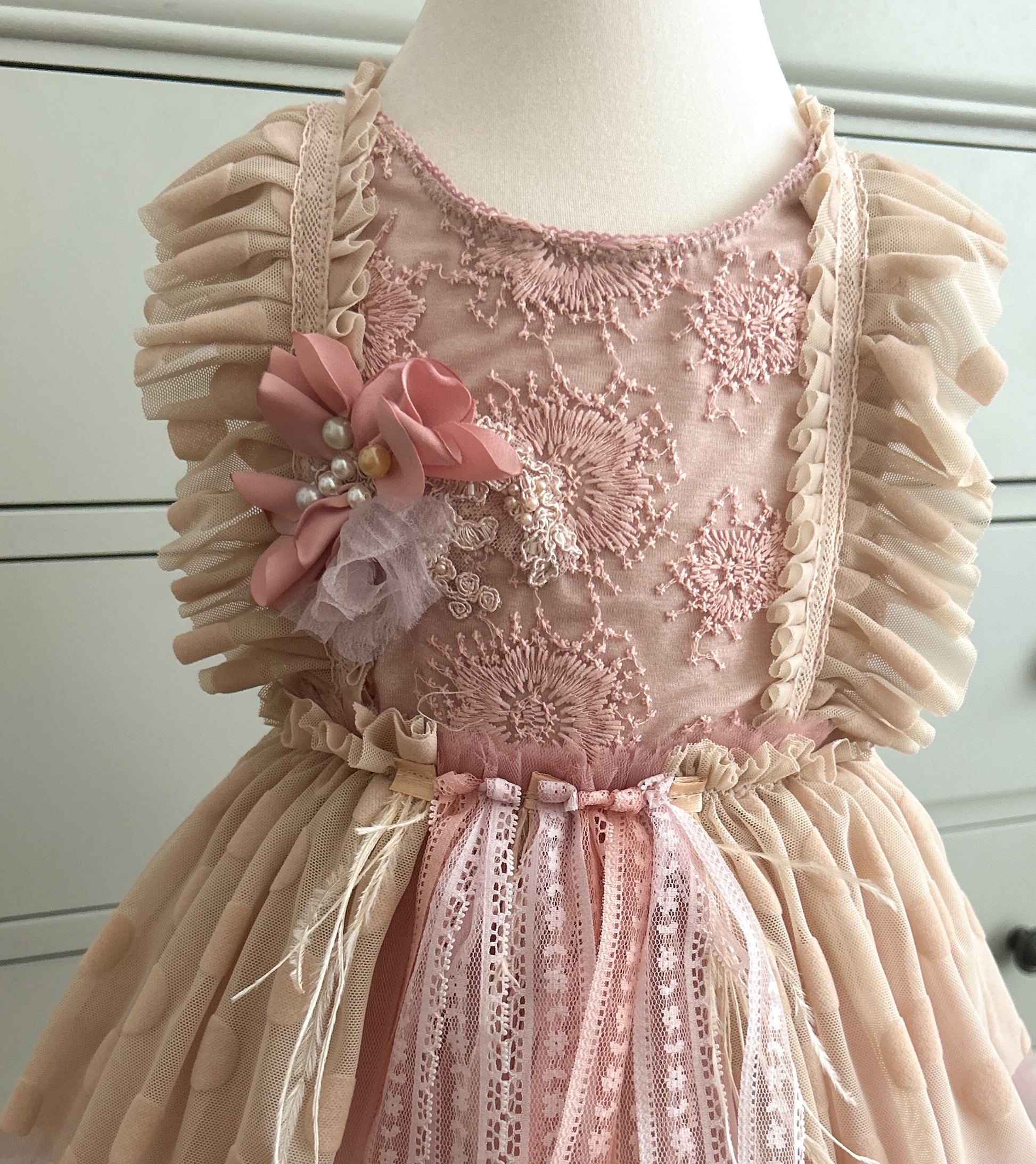 Pink lace dress with floral details on a mannequin against a white background