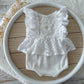 White newborn romper with ruffled lace sleeves and skirt displayed on a round tray