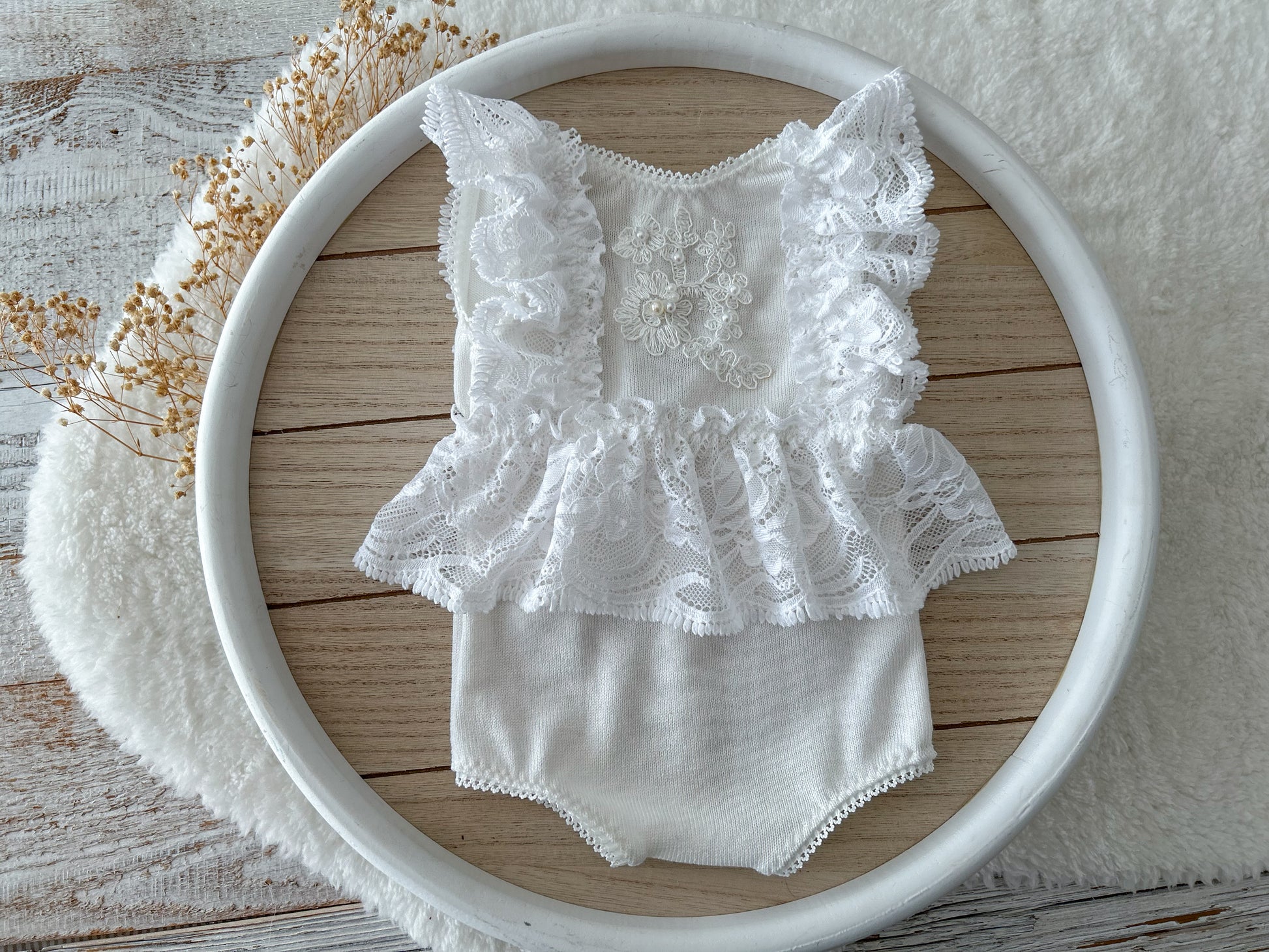 White newborn romper with ruffled lace sleeves and skirt displayed on a round tray