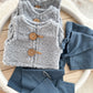 Gray knitted vest with wooden buttons and blue pants on a white circular surface.