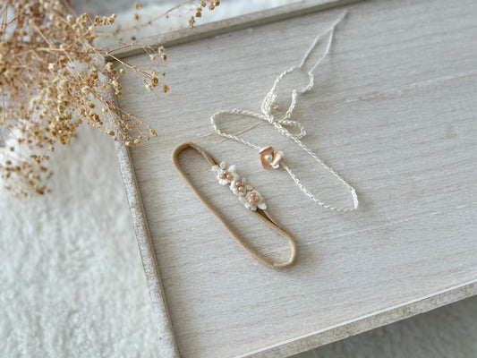 Neutral elastic baby headband with ivory flowers and blush pink pearl accents, styled flat on a wooden tray.

