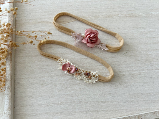 Newborn photography headbands in blush pink with floral details and lace, laid on a wooden tray