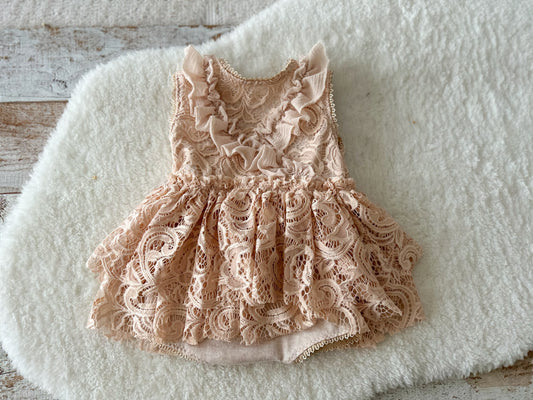 Flat lay of sitter romper dress with blush lace, ruffles, and soft lining on white background