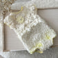 White lace baby romper with yellow accents on a wooden surface