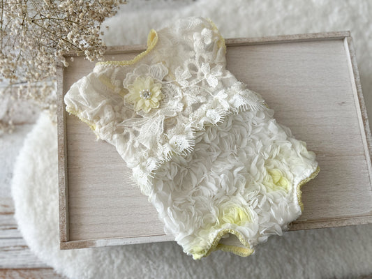 White lace baby romper with yellow accents on a wooden surface
