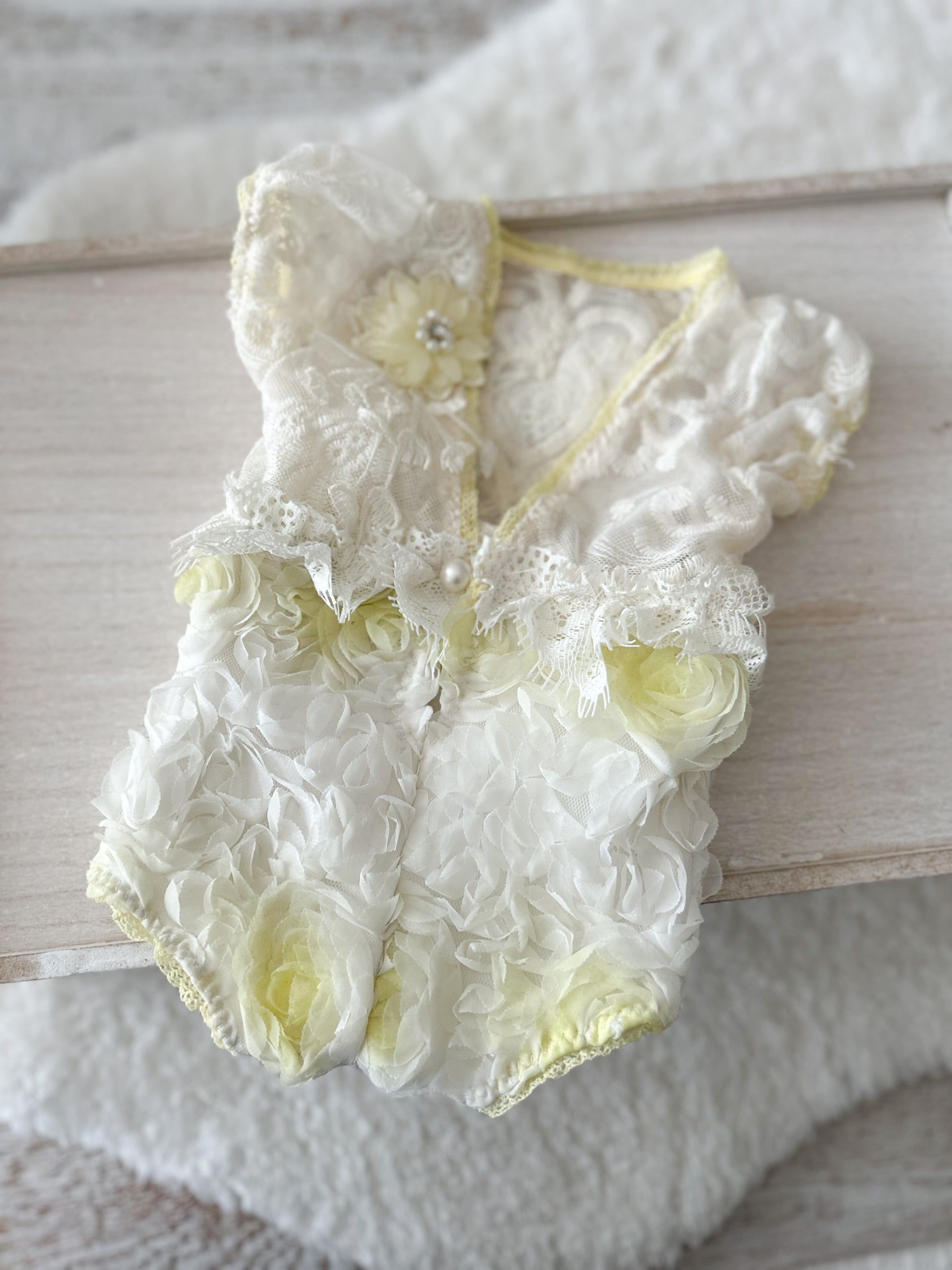 Delicate lace baby romper with floral details on a wooden surface