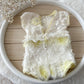 White lace baby romper for photography with yellow accents on a wooden surface