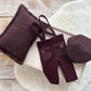 Newborn boy photo outfit in burgundy red with suspender pants, matching flat cap, and posing pillow on light wood background