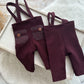 Pair of maroon suspenders with buttons on a textured surface for newborn boy photography shoots