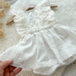 White baby romper with ruffled details held by a hand on a textured surface.