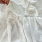 Close-up of a white baby dress with ruffled details on a wooden surface