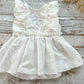 Flat lay view of white sitter romper with dotted muslin skirt and ruffled details