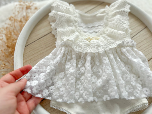 White lace dress held by a hand on a wooden surface