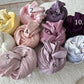 Rolled cotton swaddle wraps in 10 soft and rich tones for newborn photography, displayed on a cozy white textured surface.
