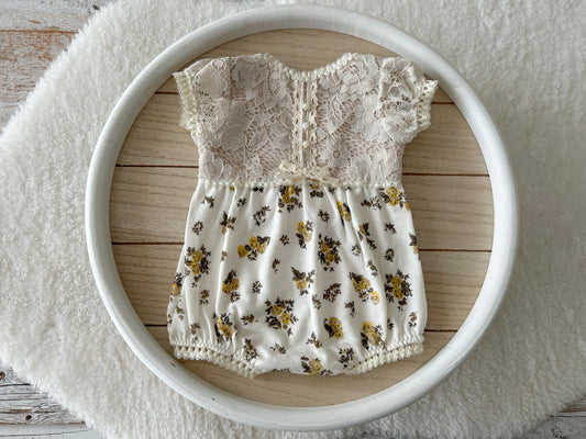 Newborn photo romper with ivory lace top and yellow floral bottom – flat lay view