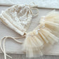Newborn lace bonnet and tutu skirt on a wooden tray.