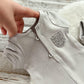 Close-up of a baby onesie with a hand adjusting the straps on a wooden surface