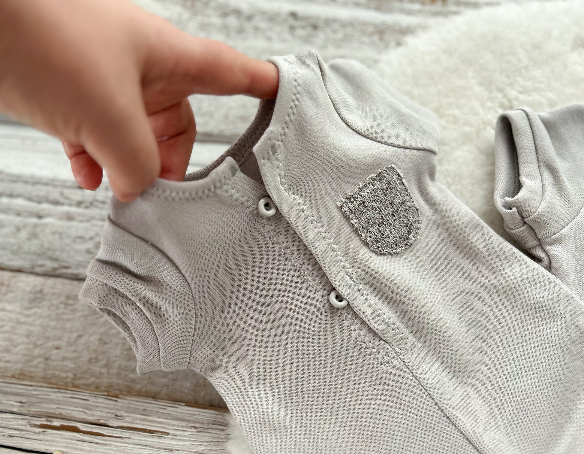 Close-up of a baby onesie with a hand adjusting the straps on a wooden surface