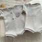 Gray baby romper with short sleeves and pants on a textured surface