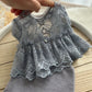 Gray lace-trimmed baby dress on a wooden surface with a blurred background