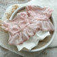 Front and back view of white and pink newborn romper with floral lace bodice and V-cut back.