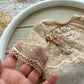 Newborn photo outfit in beige lace. Close-up of a hand holding a piece of lace fabric with floral embellishments on a wooden surface.