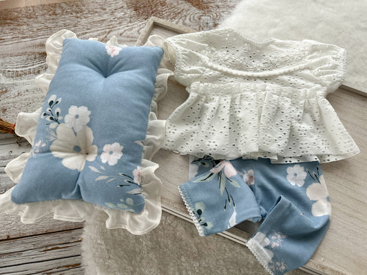 Newborn photography outfit with white top and floral pants set on wooden background