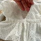 White embroidered baby girl photo outfit held by a hand on a light background
