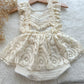 Front view of cream lace boho romper for baby girl, displayed on a soft textured surface