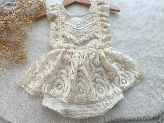 Front view of cream lace boho romper for baby girl, displayed on a soft textured surface