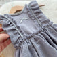 Sitter photo dress, gray dress with ruffled details held by a hand on a neutral background