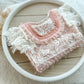 Pink lace baby outfit on a wooden surface with a white bowl