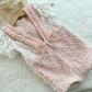 Back of pink baby romper with V-cut, pearl trim, and tied organza bows on a white textured surface.