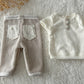 Neutral-toned newborn boy outfit displayed on wooden tray with dried flowers