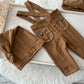 Newborn boy photo outfit with brown suspender pants and matching knot sleepy hat, laid flat on white background