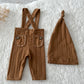 Brown newborn outfit with ribbed suspender pants and matching hat displayed on a textured cream blanket.