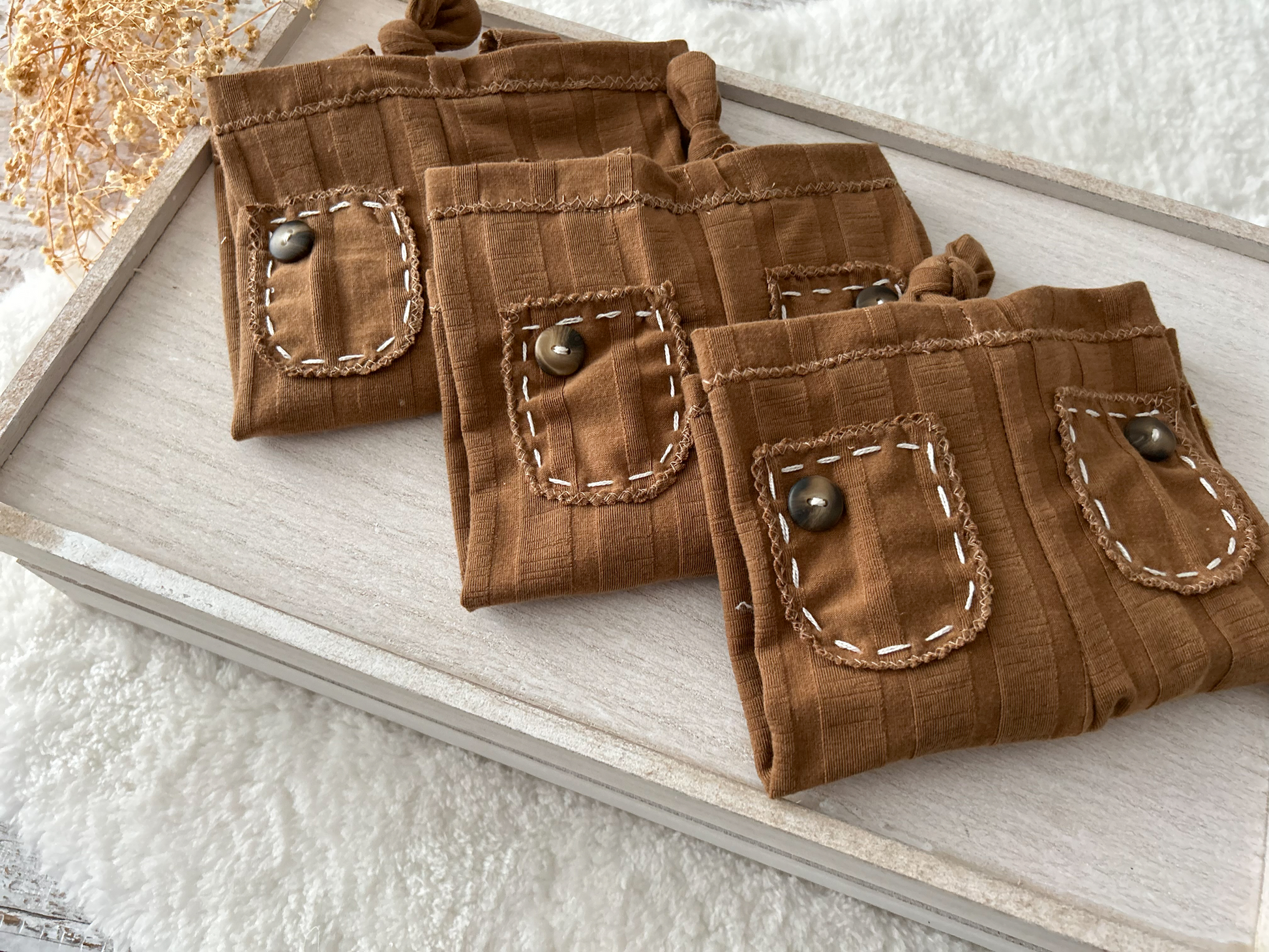 Detailed view of the brown ribbed fabric texture and hand-stitched accents on the newborn suspender pants.
