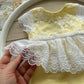 Newborn yellow lace romper with white embroidered lace skirt, displayed on wooden background