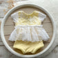 Newborn yellow lace romper with white embroidered lace skirt, displayed on wooden background