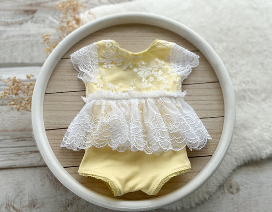Newborn yellow lace romper with white embroidered lace skirt, displayed on wooden background