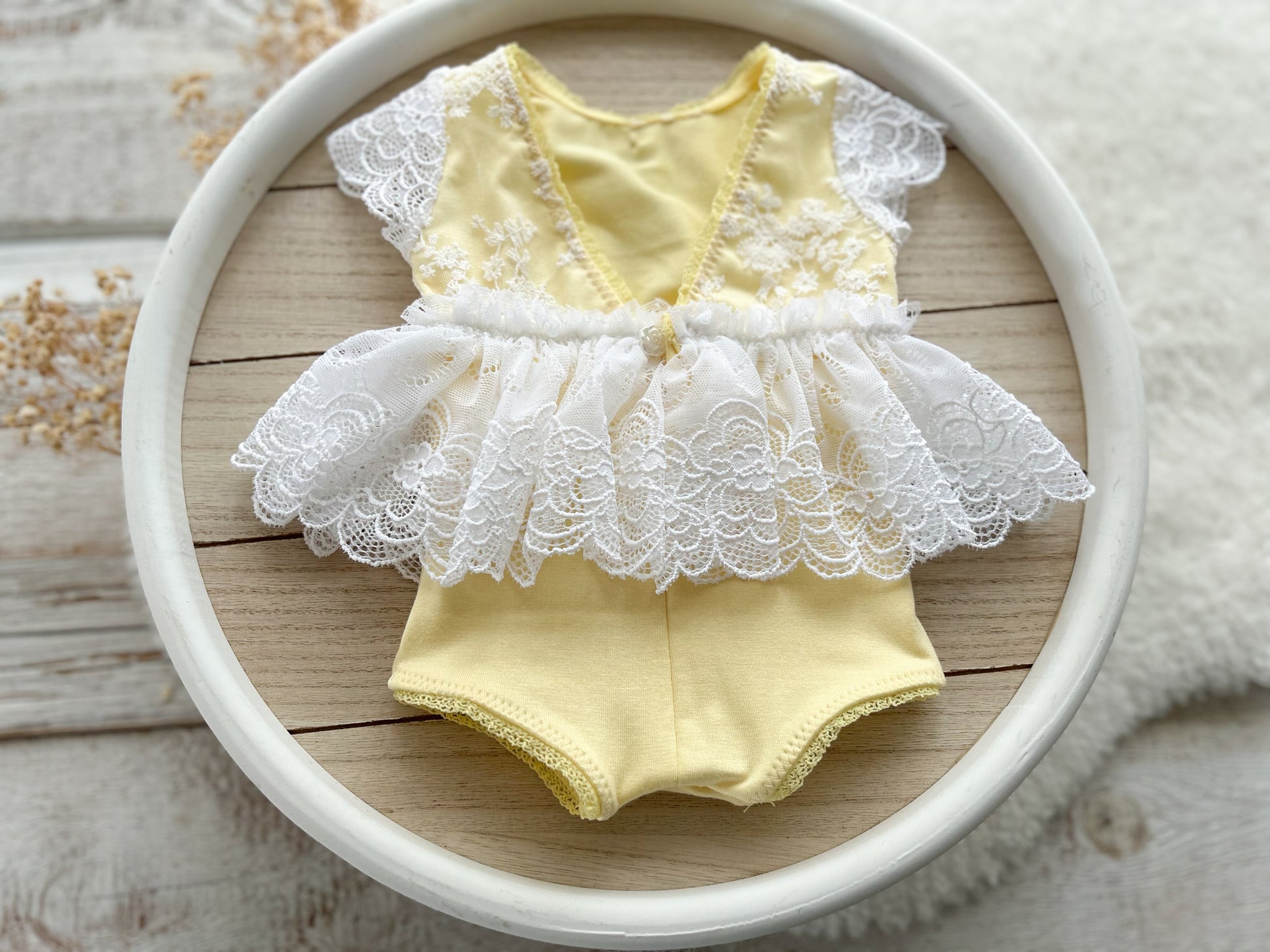 The back of newborn romper in pale yellow color with white floral lace for the skirt and top part. 