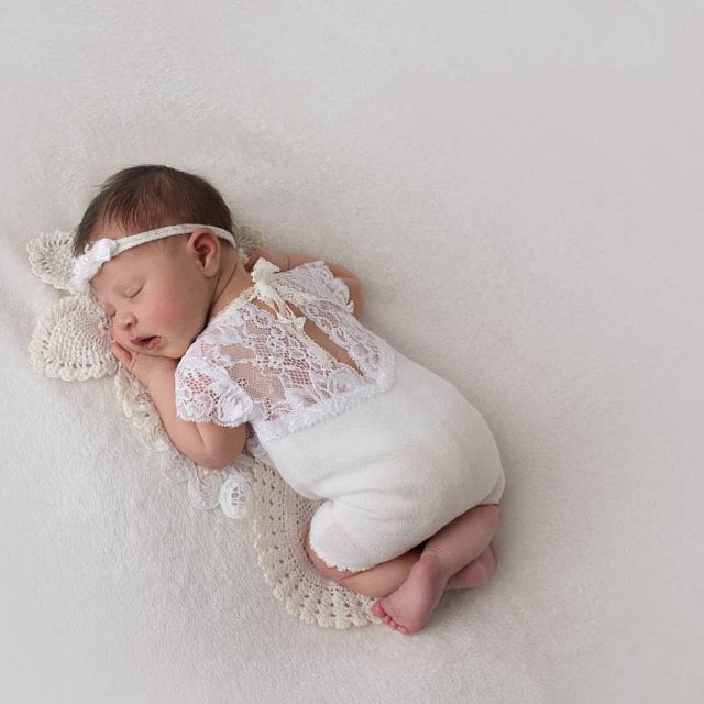 A baby girl wearing this soft newborn outfit with a V cut on the back. Looks very sweet and girly. White lace on top and white jersey on bottom.