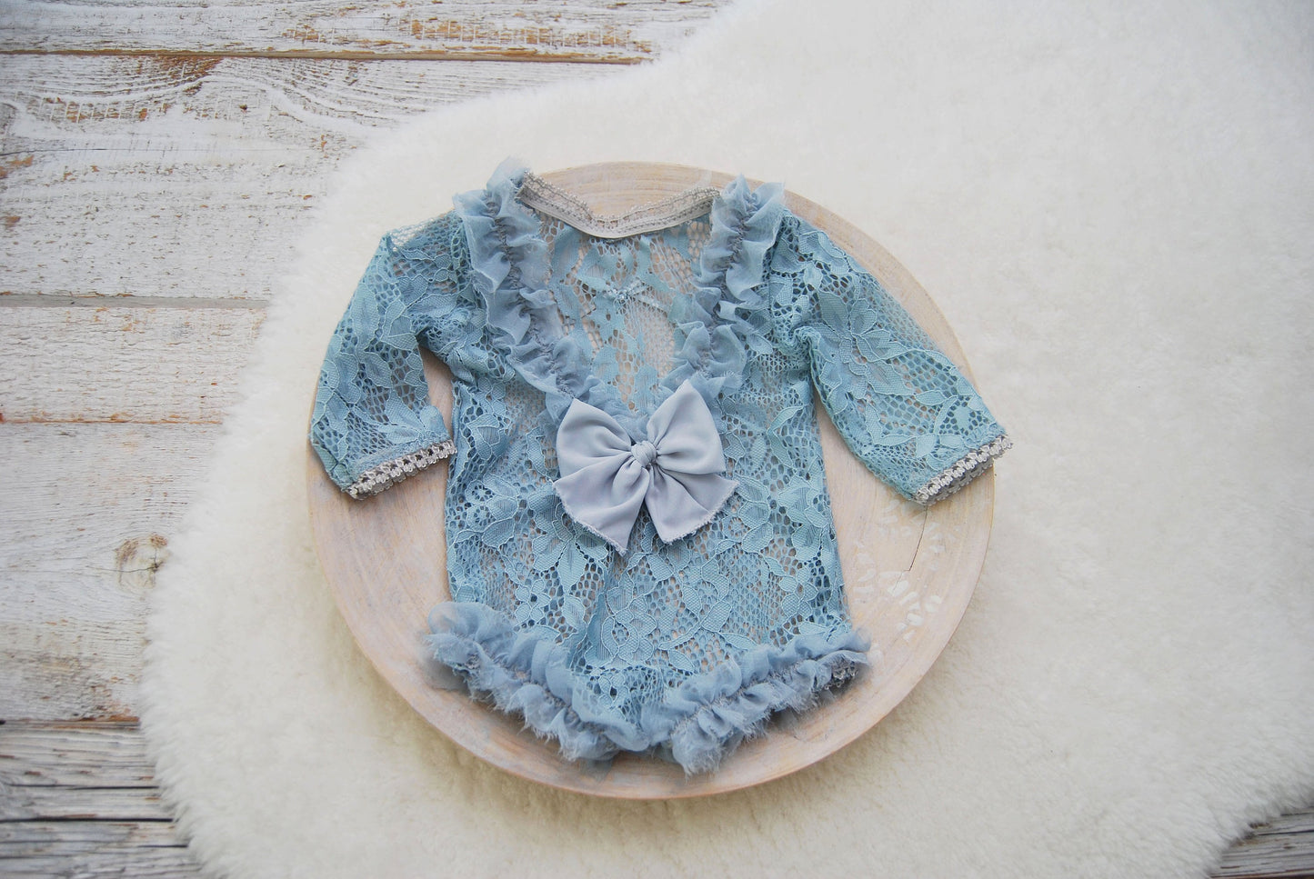 Photography prop for newborn girls. Long sleeve lace romper in blue color, with opened back, ruffles on the back and leg openings. Adorned with bow.