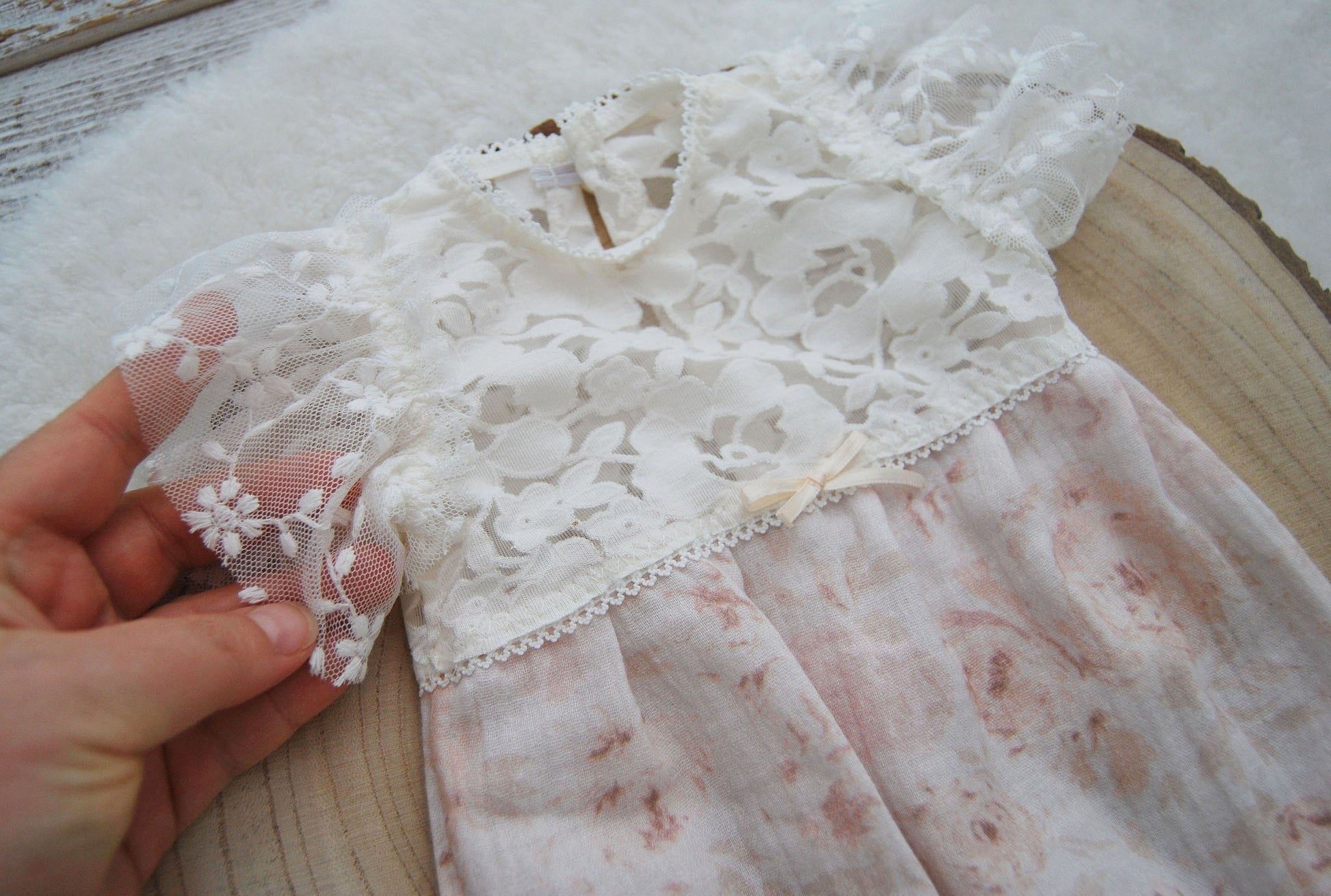 The sleeves of this newborn romper for photo shoots have made of sheer lace with small floral embroidery and are ruffled to look like little wings.