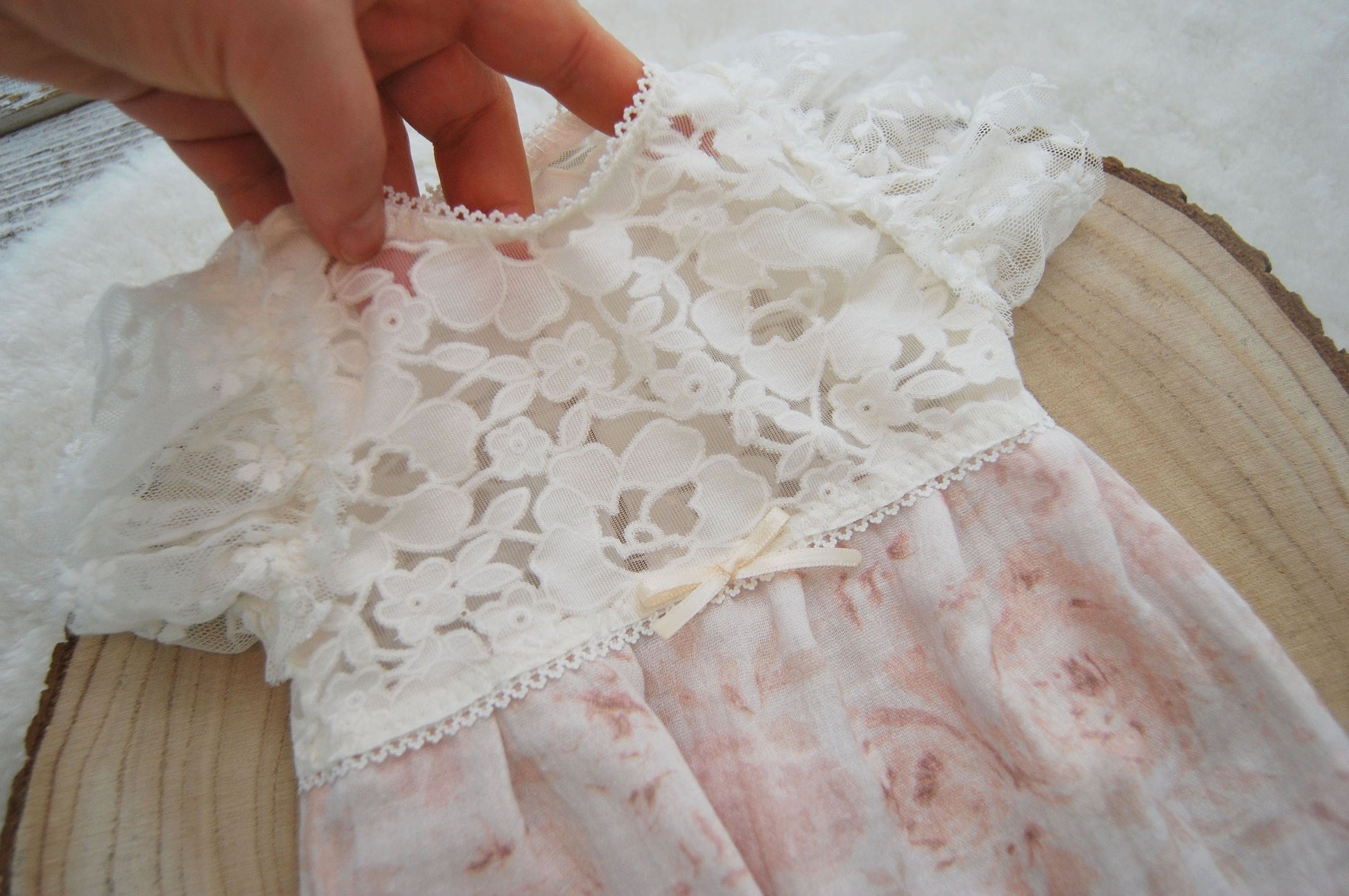 Close-up to the front top part of this newborn baby girl outfit for photo shoots. It&#39;s made of a beautiful lace in off white color, that has a floral pattern. Also decorated with little bow.